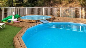 Ein Garten mit einer Holzterrasse, einem Schwimmbecken und aufblasbaren Spielzeugen.