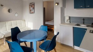 Ein kompakter Wohnbereich mit Küchenzeile, einem Essbereich mit Tisch und Stühlen, einer Couch und einem Bett im Hintergrund.