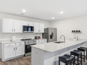 Una cocina moderna con armarios blancos, una isla central con taburetes y electrodomésticos integrados: horno, microondas y refrigerador.