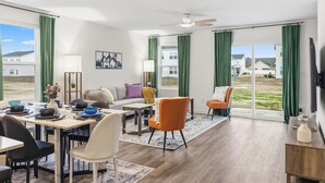 Ein modernes Wohnzimmer mit Essbereich, großen Fenstern und einem Deckenventilator.
