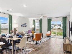 Una sala de estar moderna con comedor, ventanas amplias y un ventilador de techo.