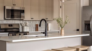 Une cuisine moderne dotée d’un îlot central, d’appareils électroménagers en acier inoxydable, de tabourets en bois et de luminaires suspendus.