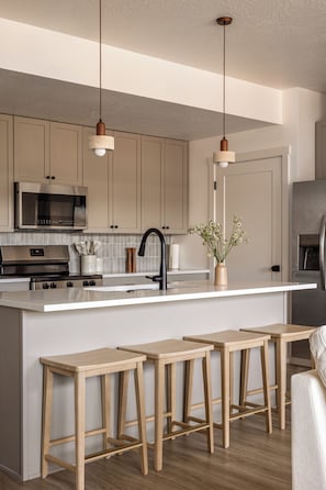 A modern kitchen with a central island, stainless steel appliances, wooden stools, and pendant lighting. - Luxury Zion Retreat • Resort Pool + Lazy River (Hurricane)