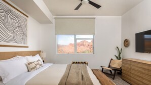 Une chambre à coucher comprenant un lit, un banc, une chaise, un téléviseur et une fenêtre donnant sur des formations rocheuses rouges.
