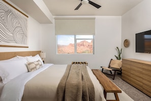 A bedroom with a bed, a bench, a chair, a TV, and a window with a view of red rock formations. - Luxury Zion Retreat • Resort Pool + Lazy River (Hurricane)