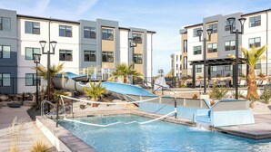 Une piscine avec un toboggan, entourée de bâtiments modernes et de palmiers.