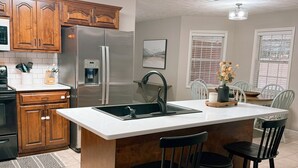 A kitchen with wooden cabinets, a stainless steel refrigerator, a built-in sink, and a bar area with stools. - Spacious County Oasis near Tupelo (Saltillo)
