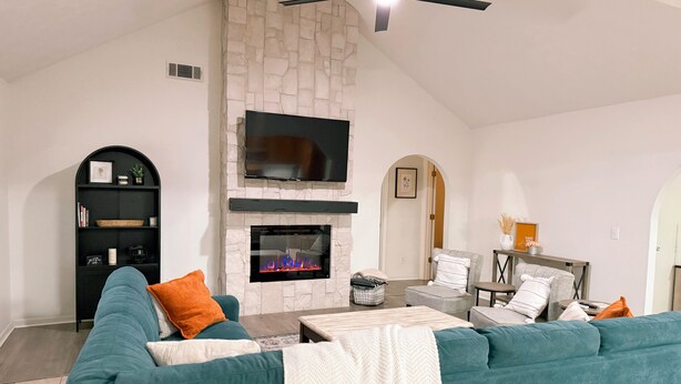 A living room with a stone fireplace, a black entertainment unit, teal sofas, and a ceiling fan. - Spacious County Oasis near Tupelo (Saltillo)