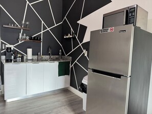 Et moderne køkken med et rustfrit stålkøleskab, en mikrobølgeovn og et geometrisk vægdesign.