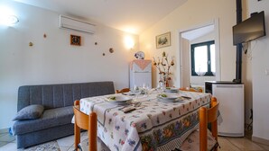 Un comedor con una mesa dispuesta para cuatro, un sofá gris, un refrigerador y una ventana con cortinas.