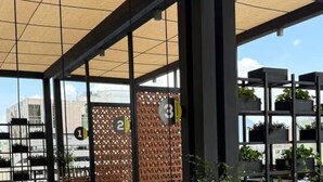 Área externa com mesas e bancos de madeira, um balanço e teto de bambu.