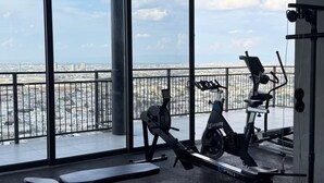 Academia com amplas janelas, equipamentos de ginástica e vista para o horizonte urbano.