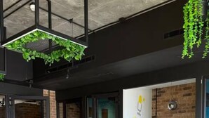 Um espaço de escritório moderno com áreas abertas e fechadas, apresentando uma parede de tijolos, um sofá amarelo e um quadro branco com anotações.
