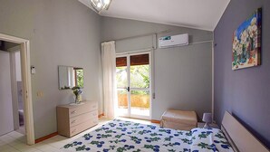 Una camera da letto con un letto, una cassettiera, una finestra con tende, un condizionatore d'aria e un quadro appeso al muro.