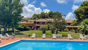 Uma piscina com espreguiçadeiras e um edifício com telhado em azulejos ao fundo.