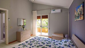 Um quarto com cama, cômoda, mesa de cabeceira, janela com cortinas e ar condicionado.