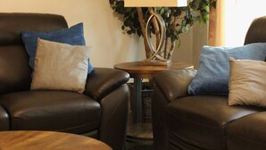 Een woonkamer met twee leren banken, een houten salontafel en een lamp op een bijzettafeltje.