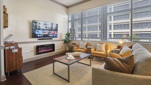 Ein modernes Wohnzimmer mit Flachbildfernseher, Kamin, bequemen Sitzgelegenheiten und großen Fenstern.