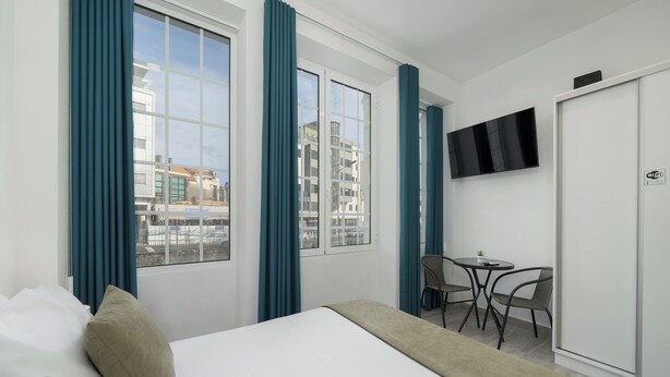 Een hotelkamer met een bed, een bureau en een stoel. Er is een televisie aan de muur en een raam met gordijnen.