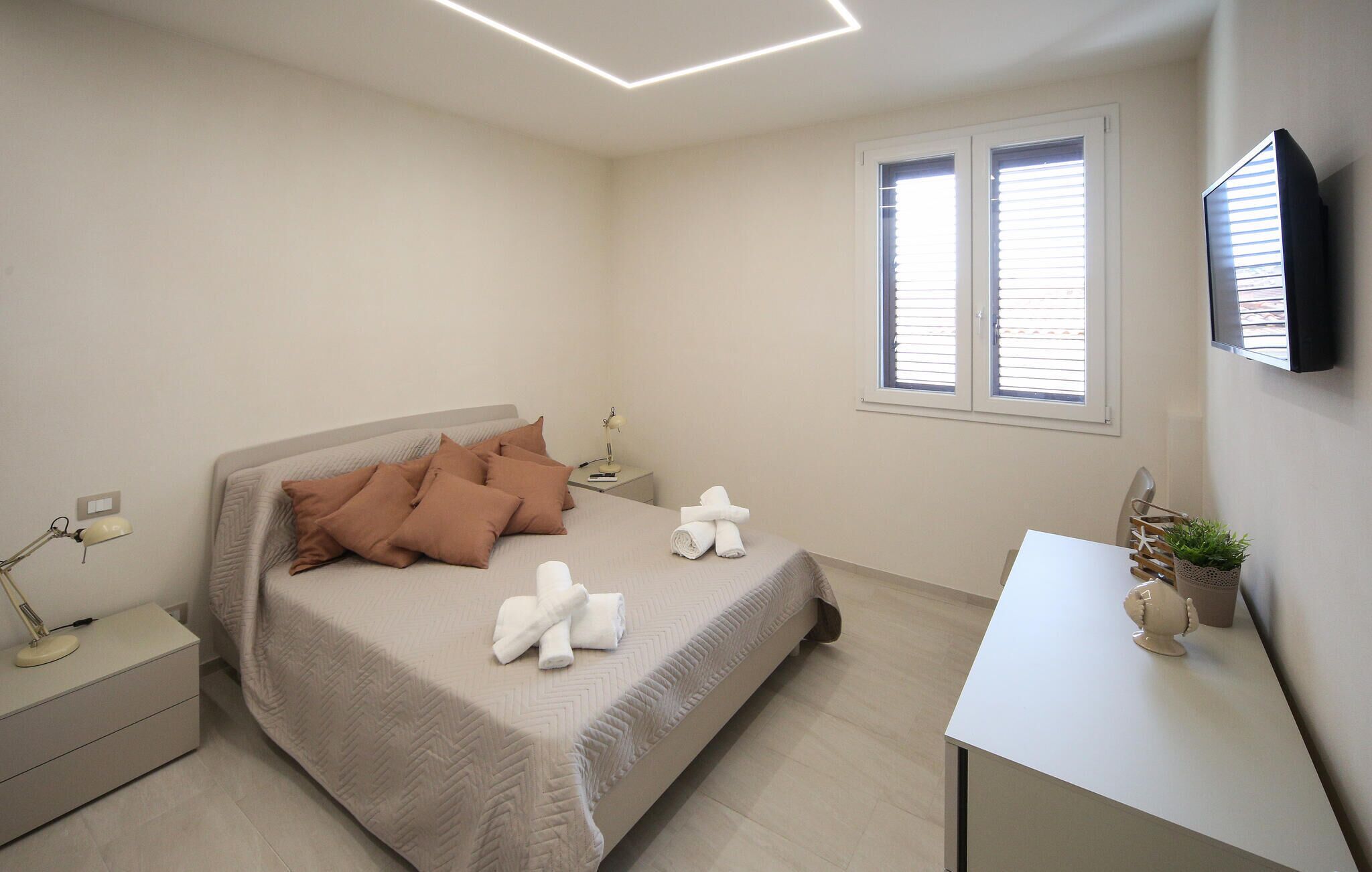 Una camera da letto moderna con un letto, due comodini, una scrivania, una TV e una finestra con persiane.