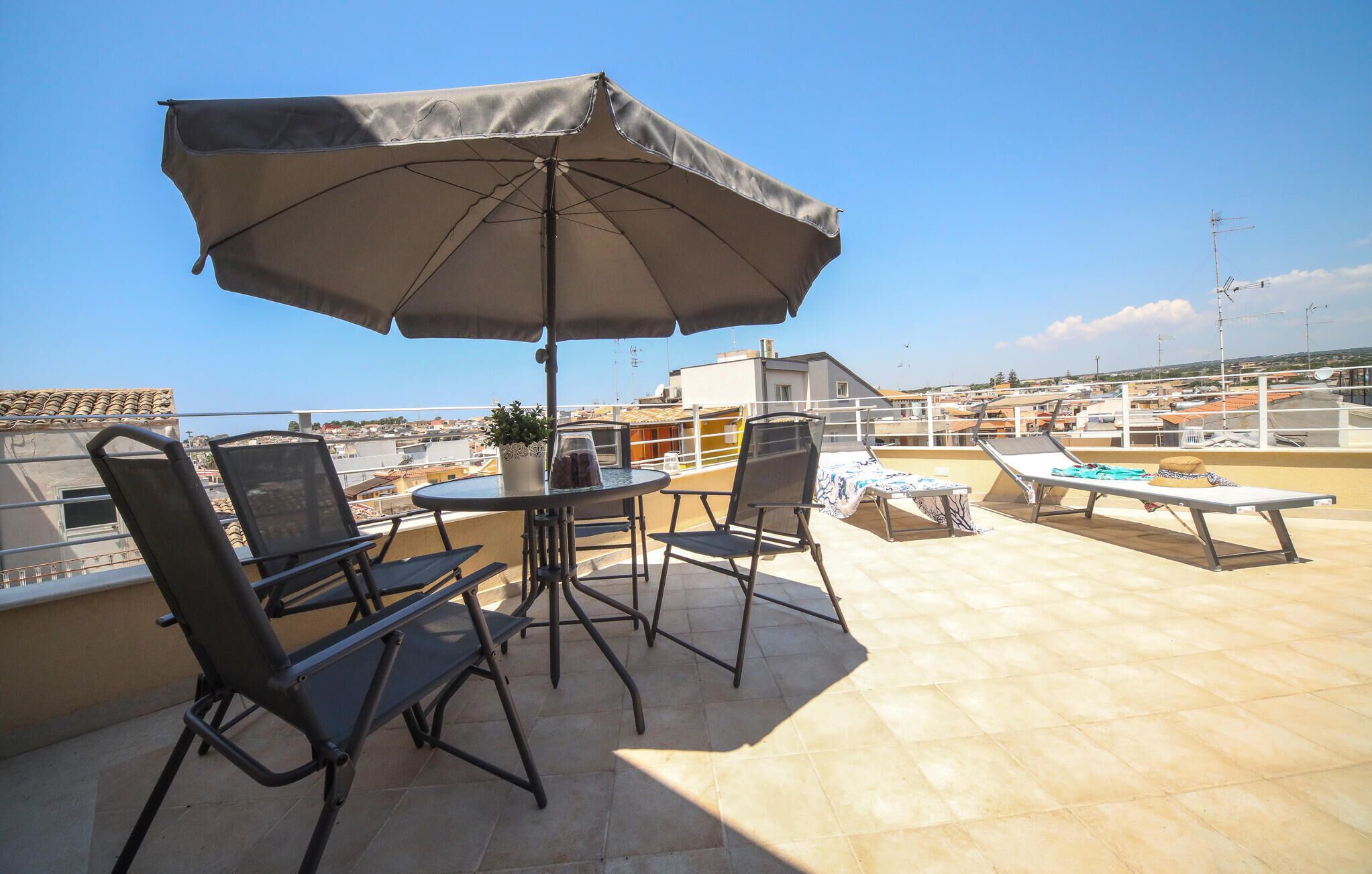 A rooftop terrace with a table, chairs, and a large umbrella.