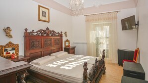 Ein Schlafzimmer mit einem hölzernen Bett, einer Kristallleuchter, einem Fernseher und einem Fenster mit Vorhängen.