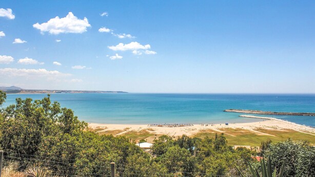 Eine Küstenlandschaft mit Strand, einem Steg und einem eingezäunten Bereich mit Vegetation.