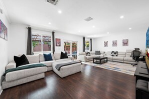 Ein geräumiges Wohnzimmer mit einem Ecksofa, einem Couchtisch und einem Schreibtisch mit Stuhl.