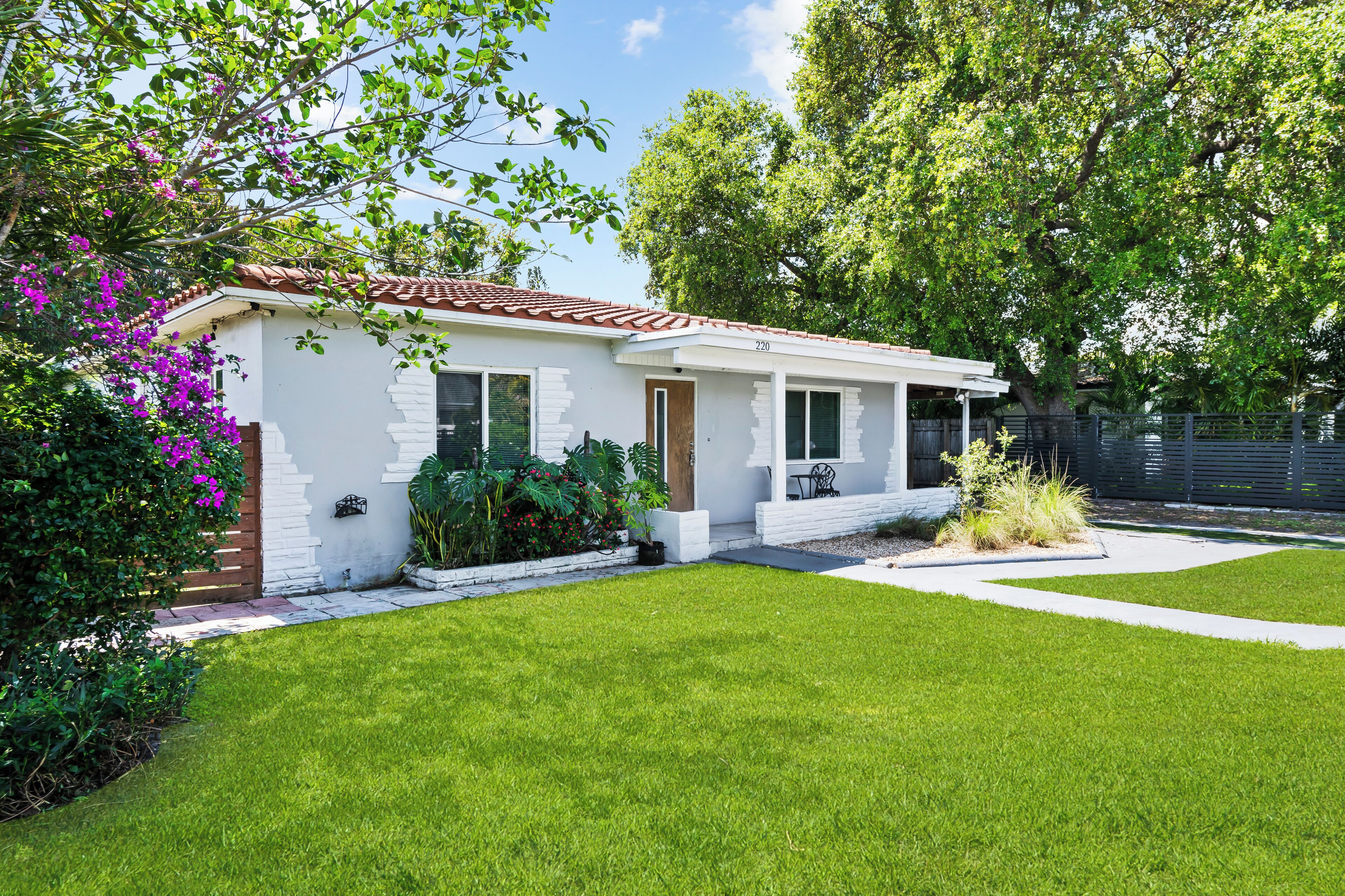A single-story house with a white exterior, a red-tiled roof, and a well-maintained lawn.