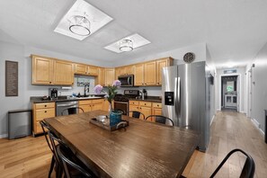 A modern kitchen with wooden cabinets, stainless steel appliances, and a dining area with a wooden table. - Torch + Timber House (Rapid City)
