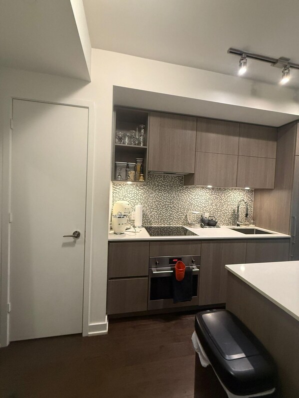 A modern kitchen with a white door, wooden cabinets, a tiled backsplash, and a stainless steel oven.