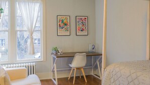 Een slaapkamer met een hemelbed, een bureau met stoel, en twee ingelijste kunstwerken aan de muur.