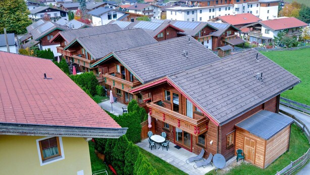 A cluster of wooden houses with red-tiled roofs, a patio with outdoor furniture, and a view of a hillside village. - Feriendorf Wildschonau-near ski Area (Wildschönau)