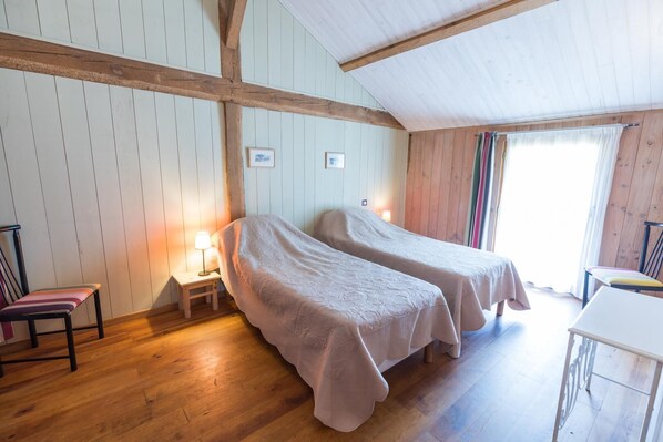 A room with two single beds, wooden floors, a small table, and a chair. - Le Pignot - GREEN - Gîte (VERT)