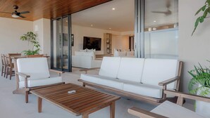 Una sala moderna con una mesa de centro de madera, sofás blancos y una puerta de vidrio que da a una cocina.