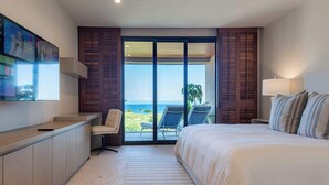 Una habitación de hotel con cama, escritorio, silla, televisión y vista al océano.