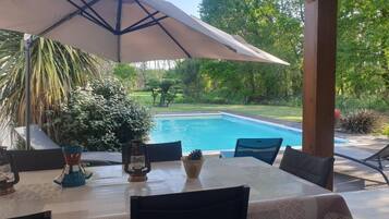 Eine Terrasse mit Tisch, Stühlen und einem großen Sonnenschirm, mit Blick auf einen Swimmingpool.