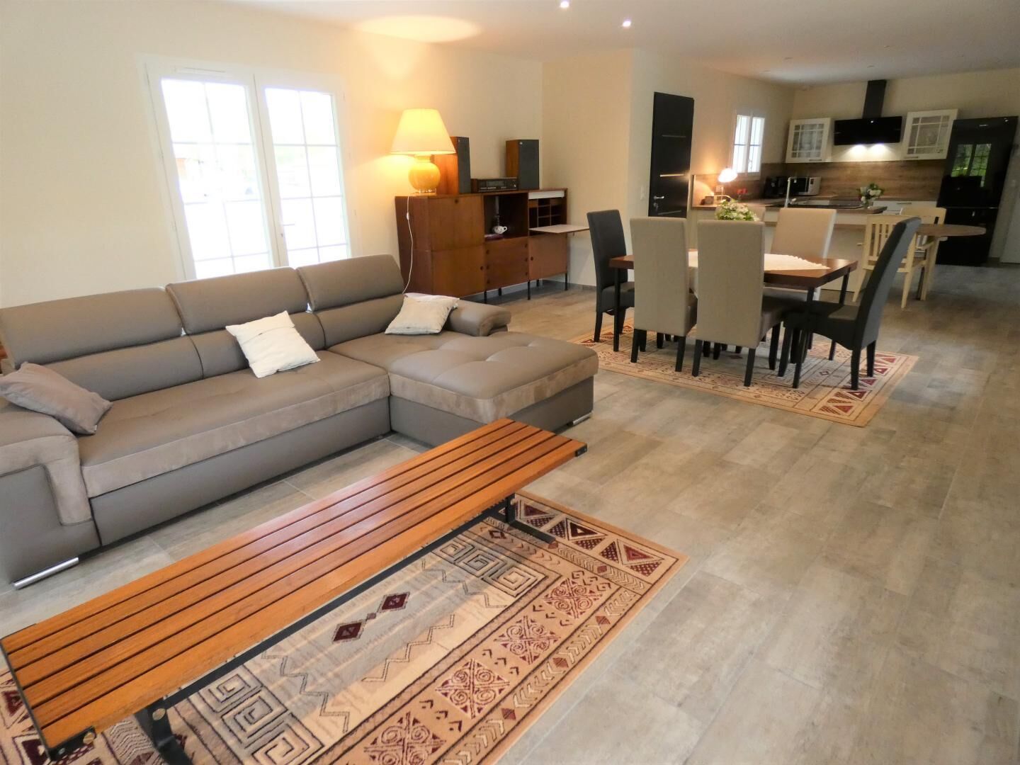Ein modernes Wohnzimmer mit einer grauen Eckcouch, einem Holztisch und einem Essbereich mit Tisch und Stühlen.