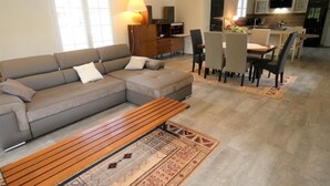 En moderne stue med en grå modulsofa, et træbord og et spiseområde med bord og stole.