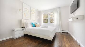 A modern bedroom with a large bed, white walls, and a window with curtains.
