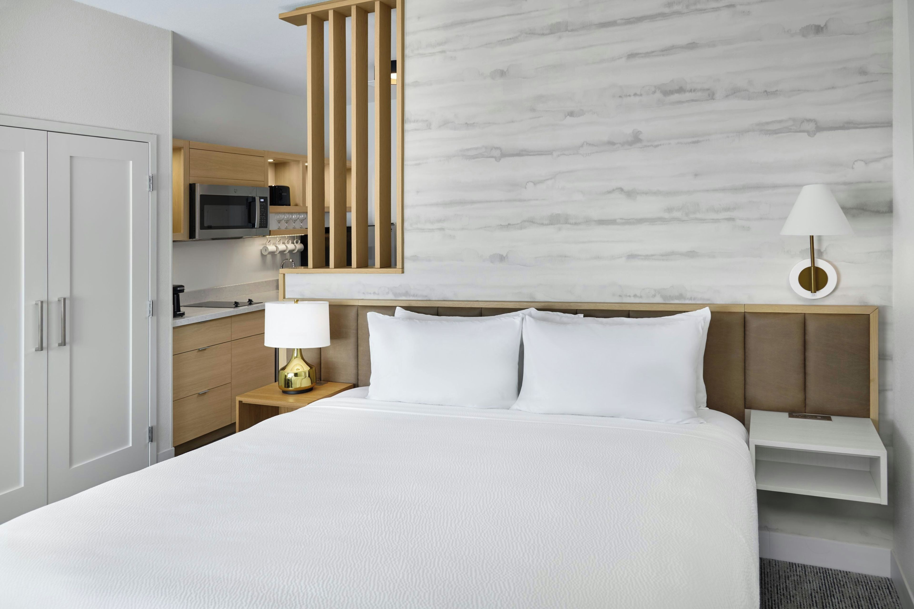 A hotel room with a bed, a nightstand, a lamp, a microwave, and a minibar.