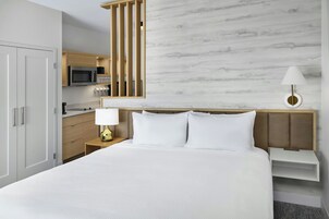 Una habitación de hotel con una cama, una mesita de noche, una lámpara, un microondas y un minibar.