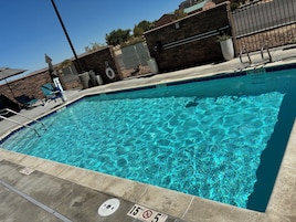 Una piscina rectangular con agua azul cristalina, un letrero que indica presencia de salvavidas y un letrero que prohíbe el clavado.
