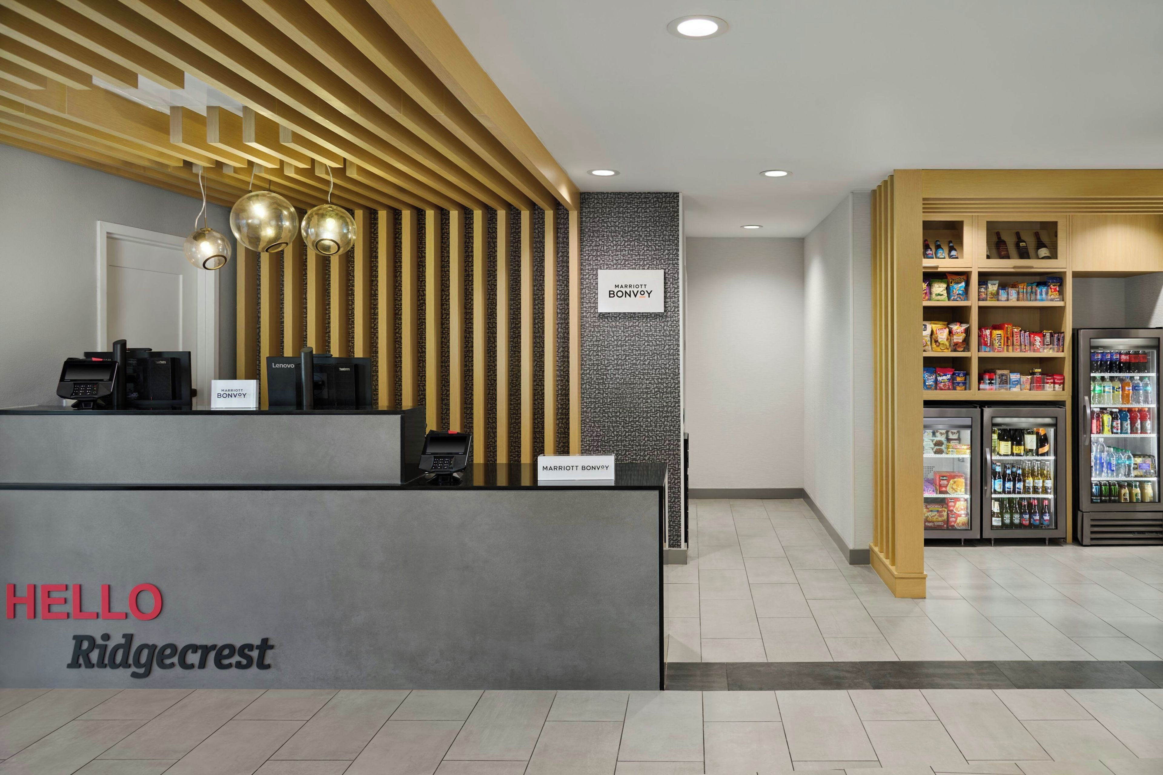 A hotel reception area with a modern design, including a reception desk, a wall-mounted sign, and a beverage refrigerator.
