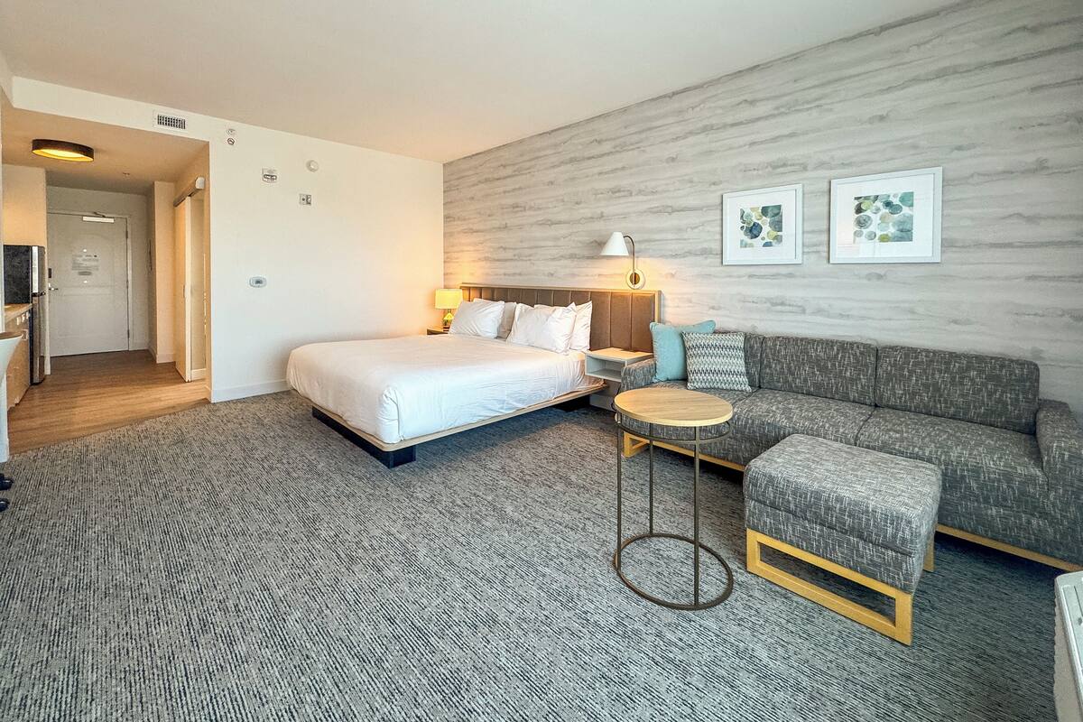 A hotel room with a bed, a sofa, a small round table, and a wall-mounted lamp.