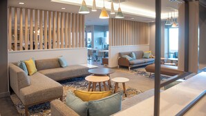 A modern hotel lobby with a sectional sofa, round tables, and a wooden partition. - Towneplace Suites By Marriott Ridgecrest (Ridgecrest)