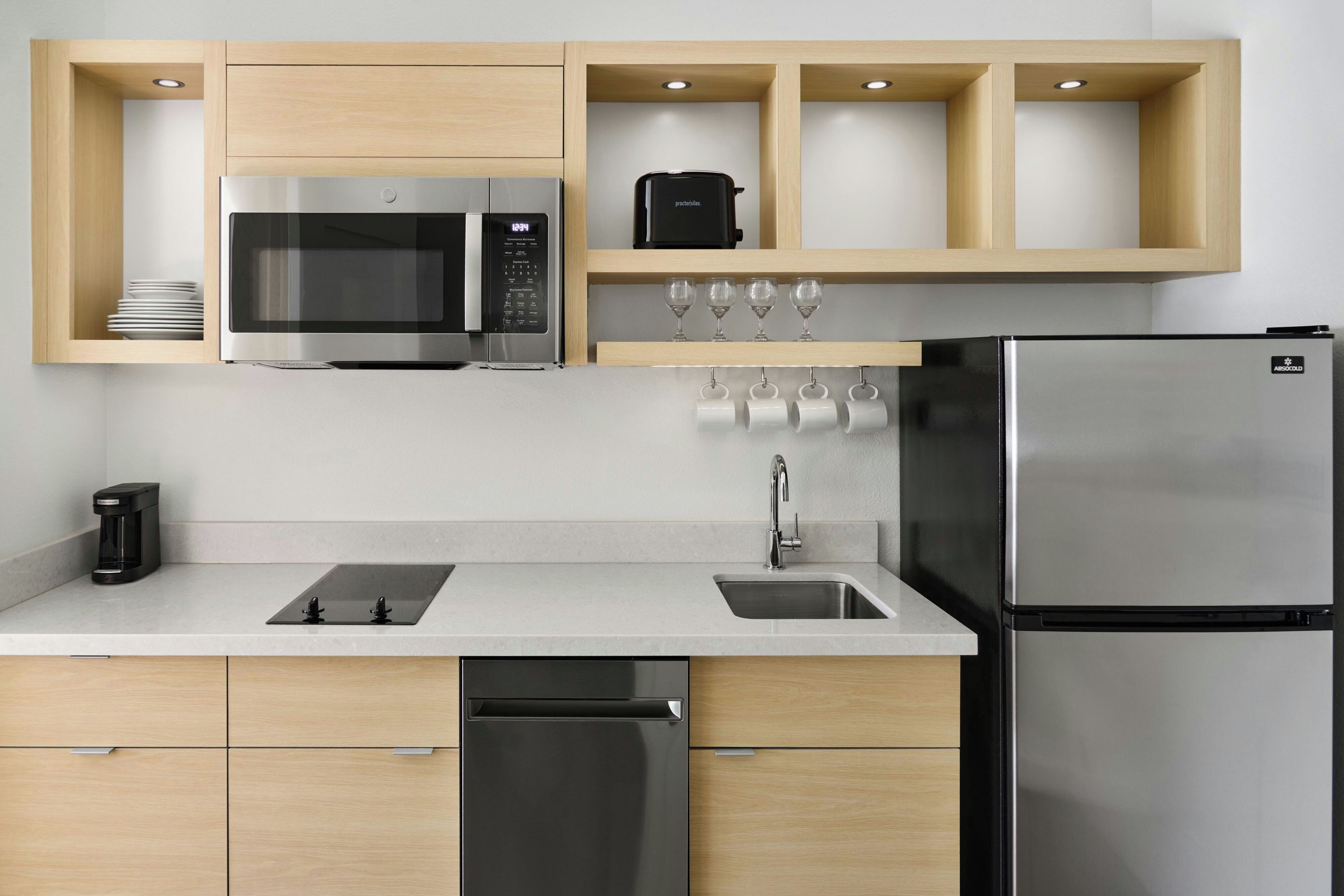 Una cocina moderna con un refrigerador de acero inoxidable, un microondas integrado, una cafetera y un lavamanos con grifo.