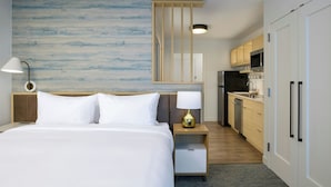 A hotel room with a bed, bedside lamp, nightstand, and a view of the kitchen area. - Towneplace Suites By Marriott Ridgecrest (Ridgecrest)