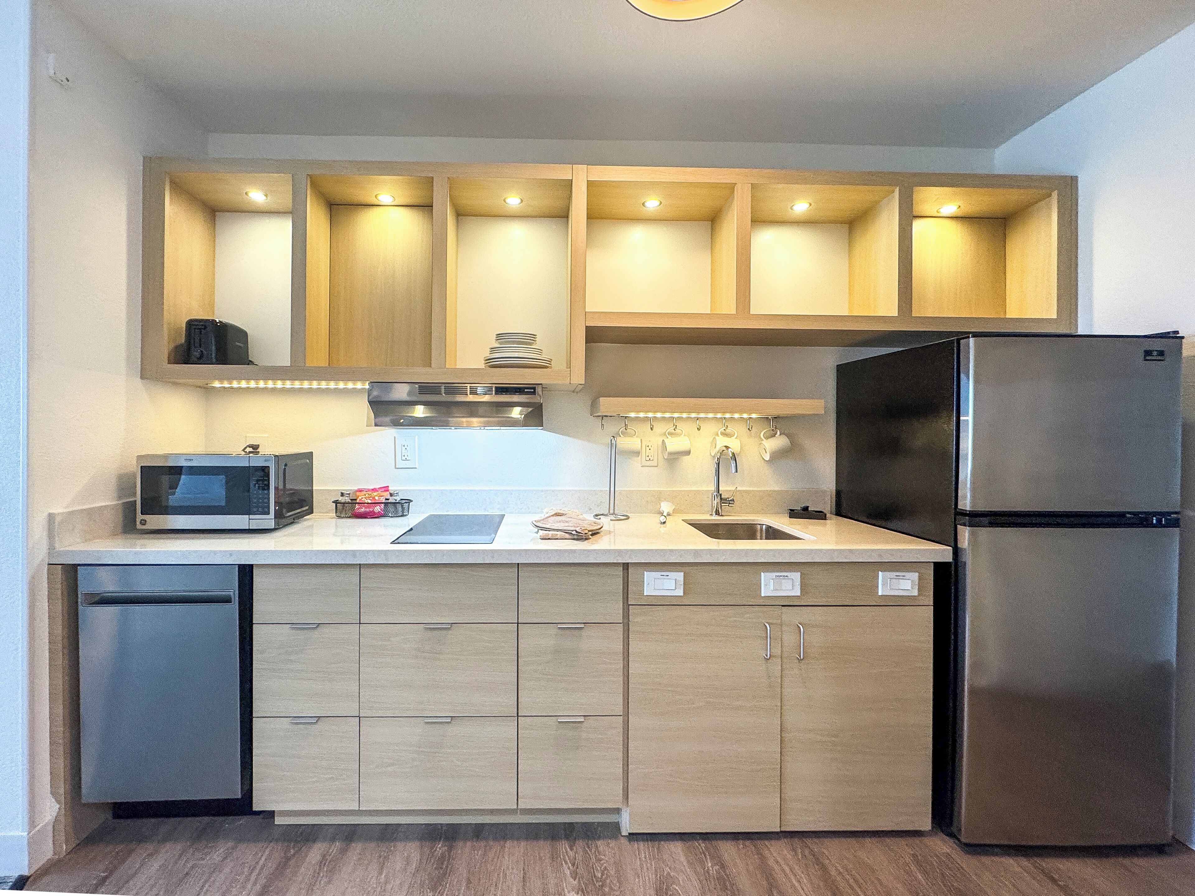 A compact kitchen with built-in appliances, wooden cabinets, and a stainless steel refrigerator.