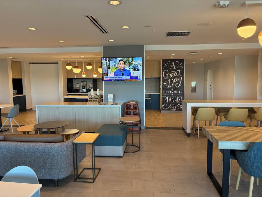 Un moderno vestíbulo de hotel con una zona de bar, asientos y un televisor mostrando un noticiero.